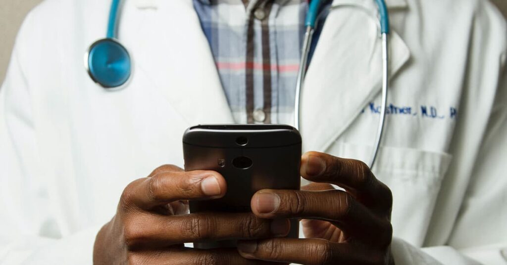 The image depicts a healthcare professional, likely a doctor or nurse, holding a mobile