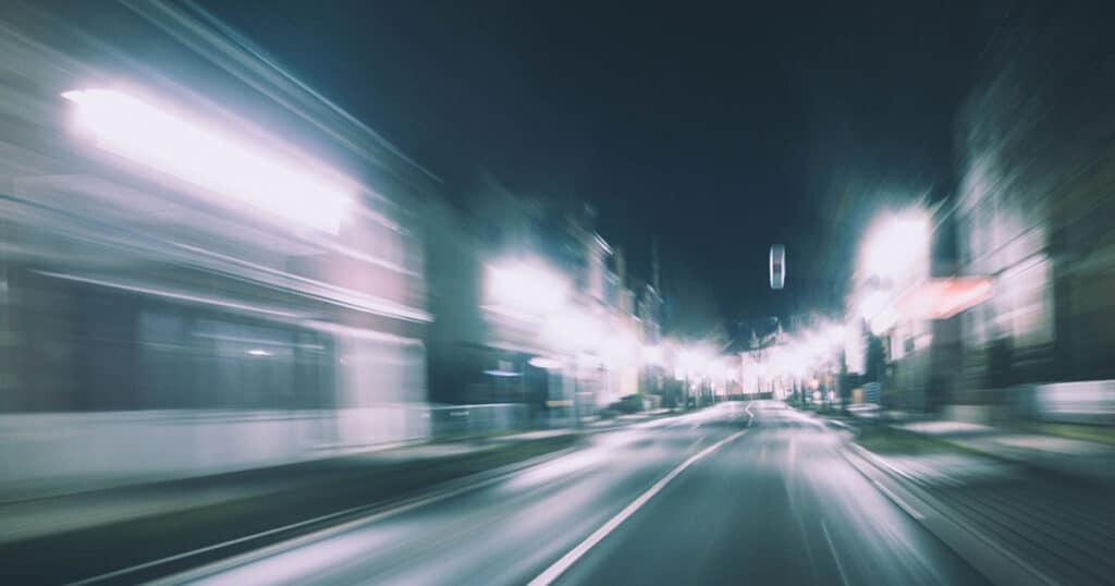 A blurred image of a road at night, with streaks of light from passing cars and streetlights, creating a sense of motion and speed.