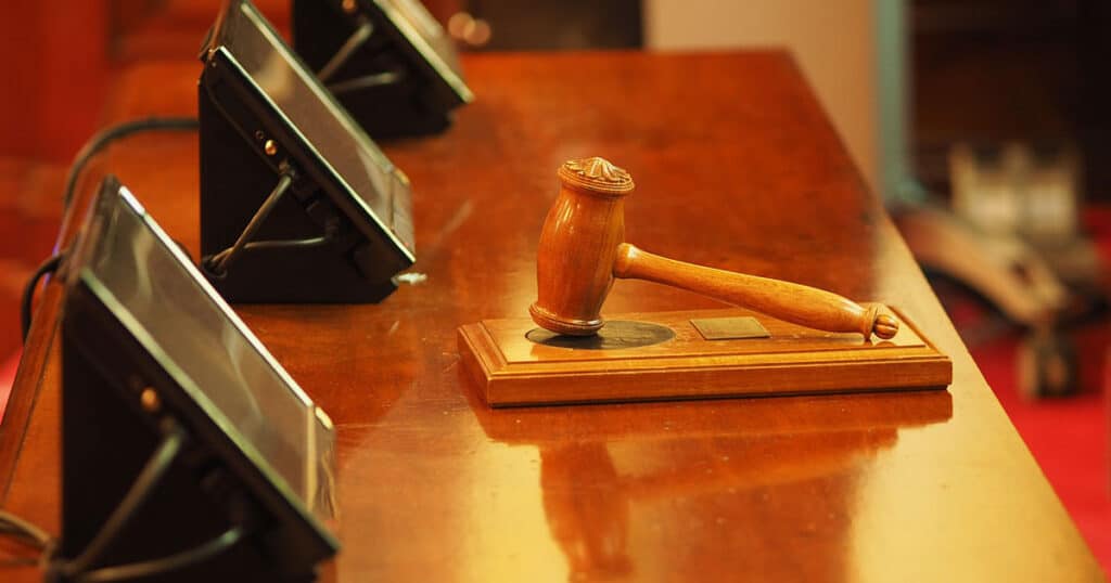 A judge's gavel resting on a wooden table in a courtroom, with microphones in the background.