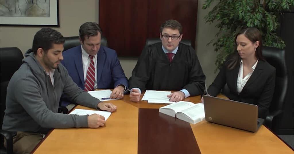 Judge, attorney, and clients seated together at a table, engaged in a legal discussion.