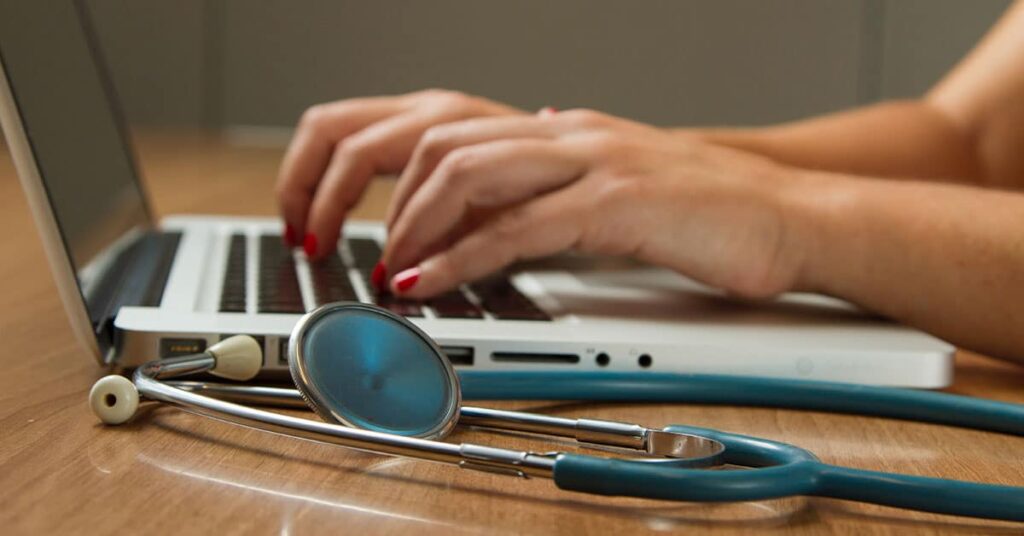 The image depicts a healthcare professional, likely a doctor or nurse, working on a laptop.