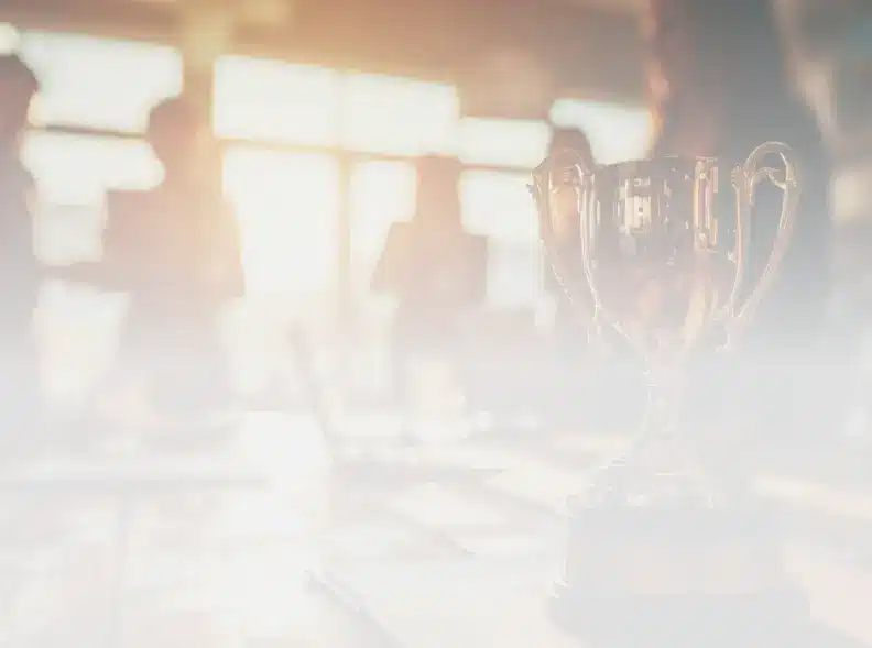 A trophy sits on a table in a brightly lit room, with people blurred in the background.